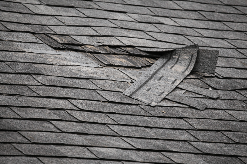 Roof with missing shingles and visible storm damage being repaired after strong winds in Texas