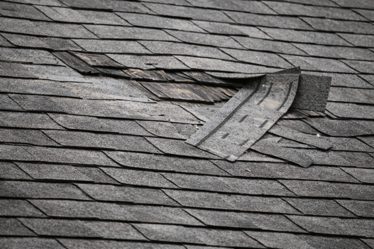 Roof with missing shingles and visible storm damage being repaired after strong winds in Texas