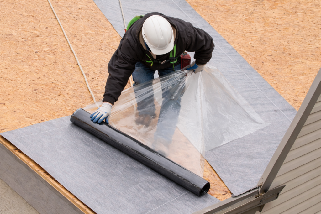 Roofing contractor installing TAMKO ice and water shield membrane on roof decking during replacement