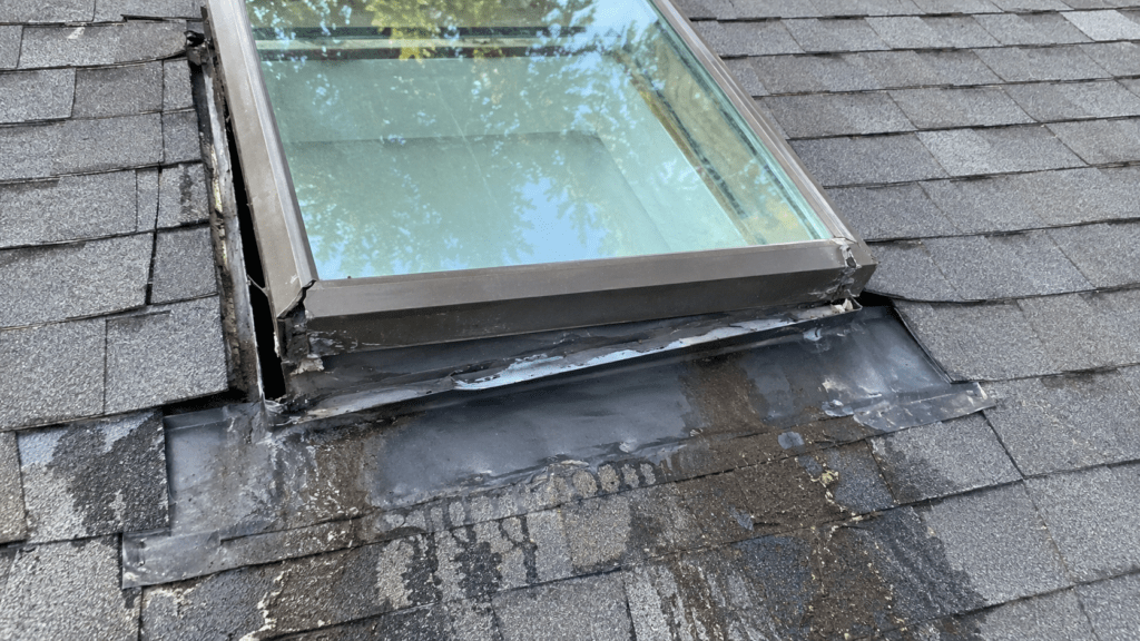 Poor skylight installation with uneven flashing, gaps around the frame, sloppy sealant, and moisture staining on a shingle roof