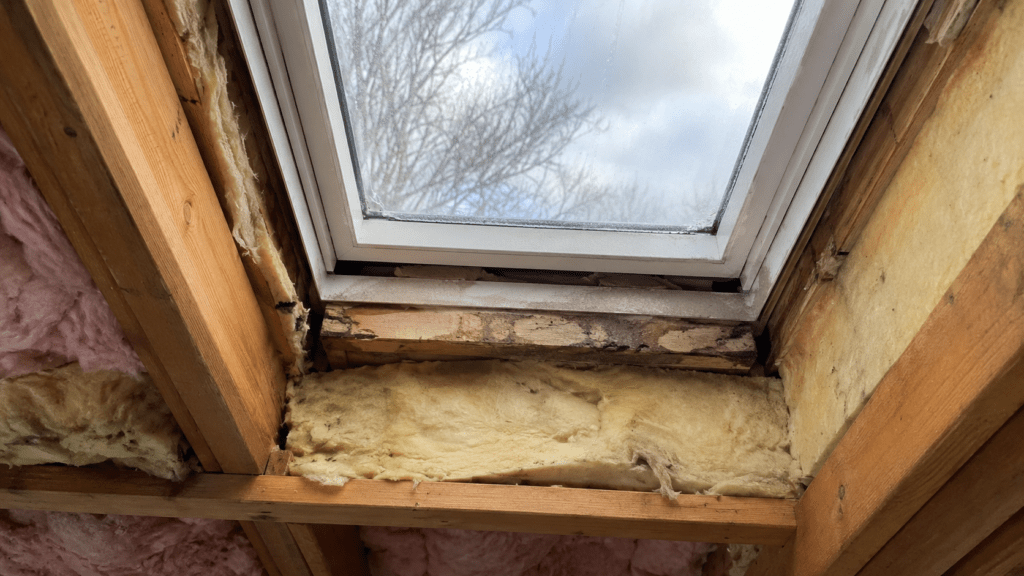 Skylight insulation problem with exposed framing, uneven fiberglass insulation, gaps around the skylight shaft, and moisture staining near the frame