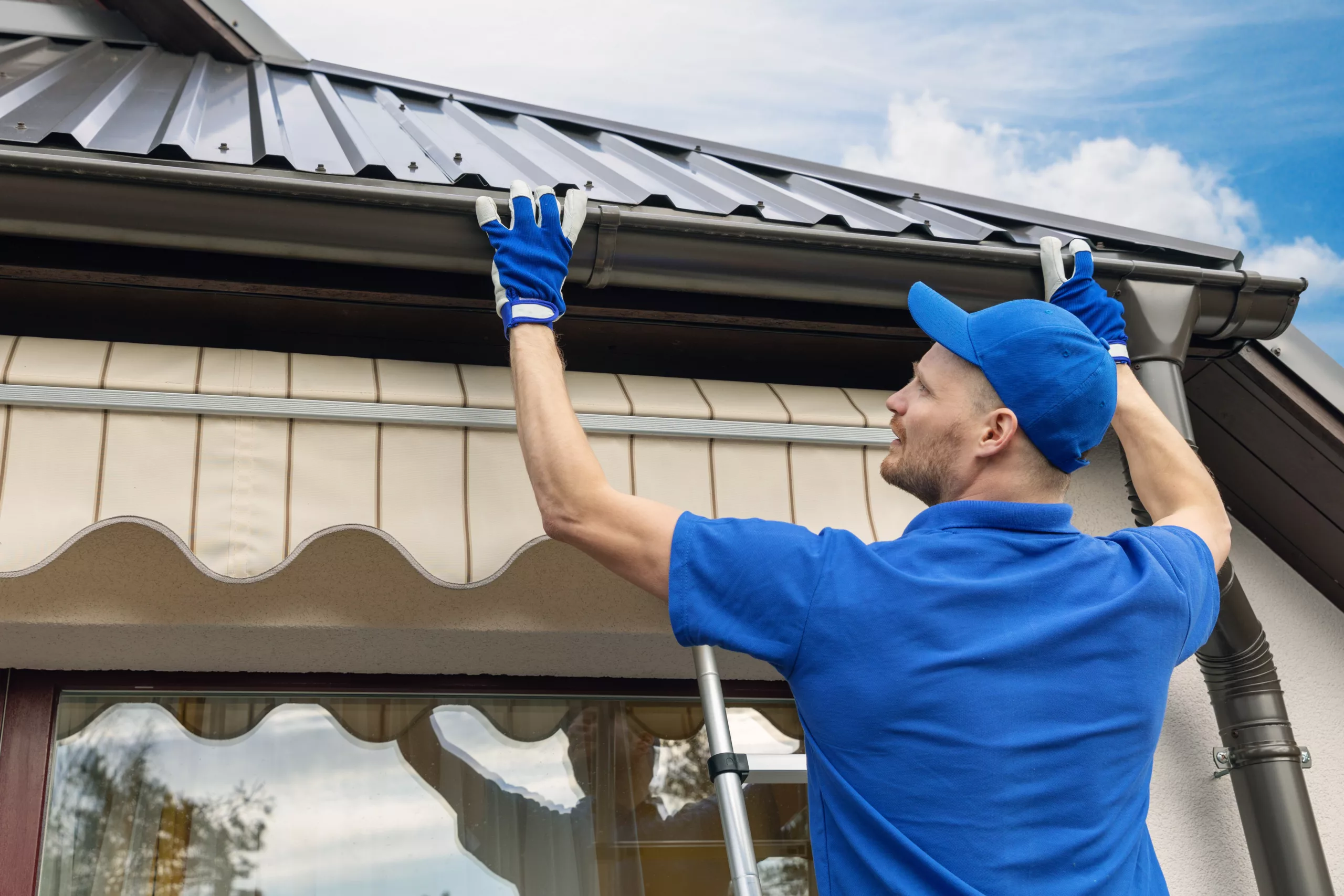Worker in blue shirt and blue hat installing a gutter system