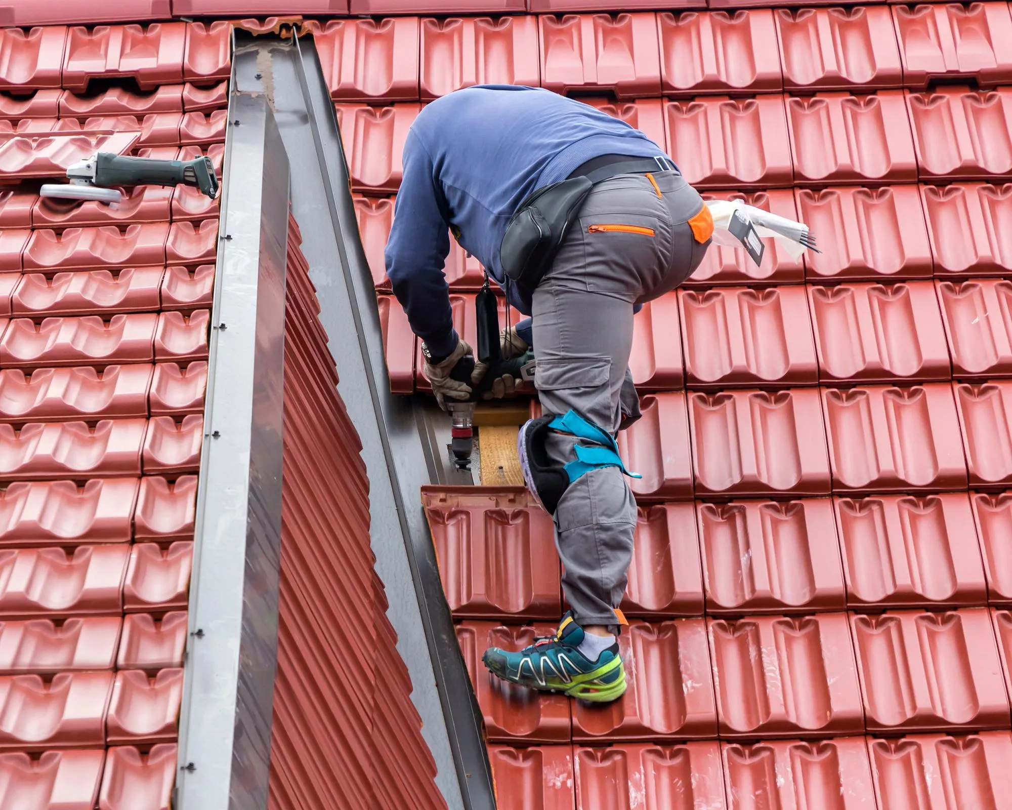 best-hail-damage-inspection-marble-falls-legacy – Legacy Roofing Pros A roofing contractor is standing on a sloped red, metal roof inspecting it for damage and making minor repairs