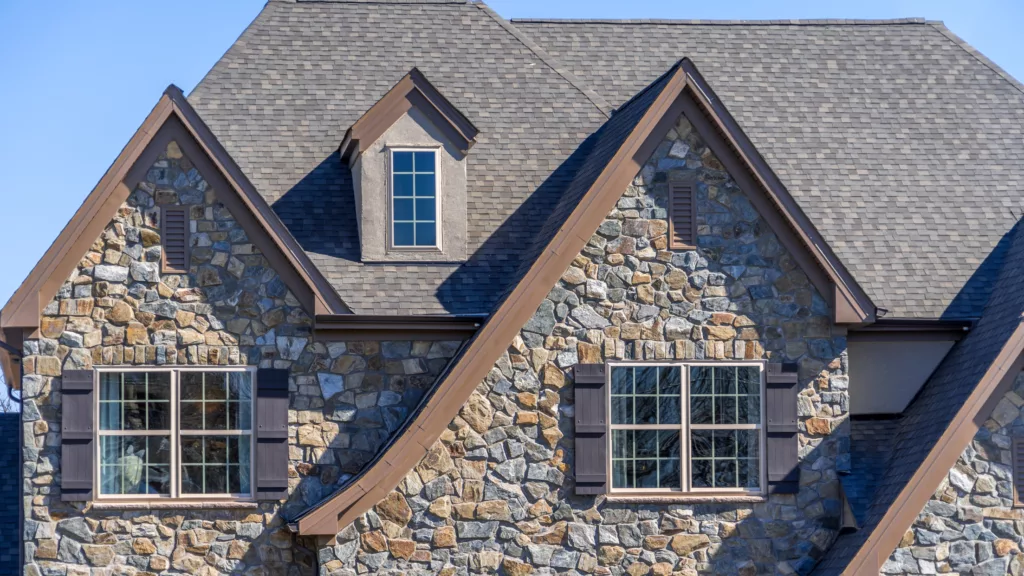 A large, luxury home with asphalt shingle roof and stone siding
