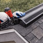 Roofing contractor installing ridge vent on shingle roof during roof replacement