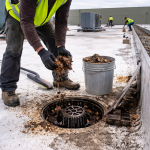 Worker applying roof coating on a flat commercial roof using a hose and spreader tool