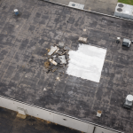 Aerial view of a commercial flat roof with emergency repair patch and storm damage debris