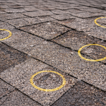 Close-up of asphalt shingle roof with hail damage marked in yellow chalk for insurance claim documentation