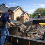 Roof material removal and disposal in Texas with roofing crew safely removing old shingles and loading debris into a dumpster