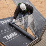 Roofing contractor installing synthetic underlayment and ice and water shield in roof valley section on plywood decking