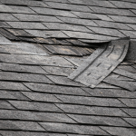 Roof with missing shingles and visible storm damage being repaired after strong winds in Texas