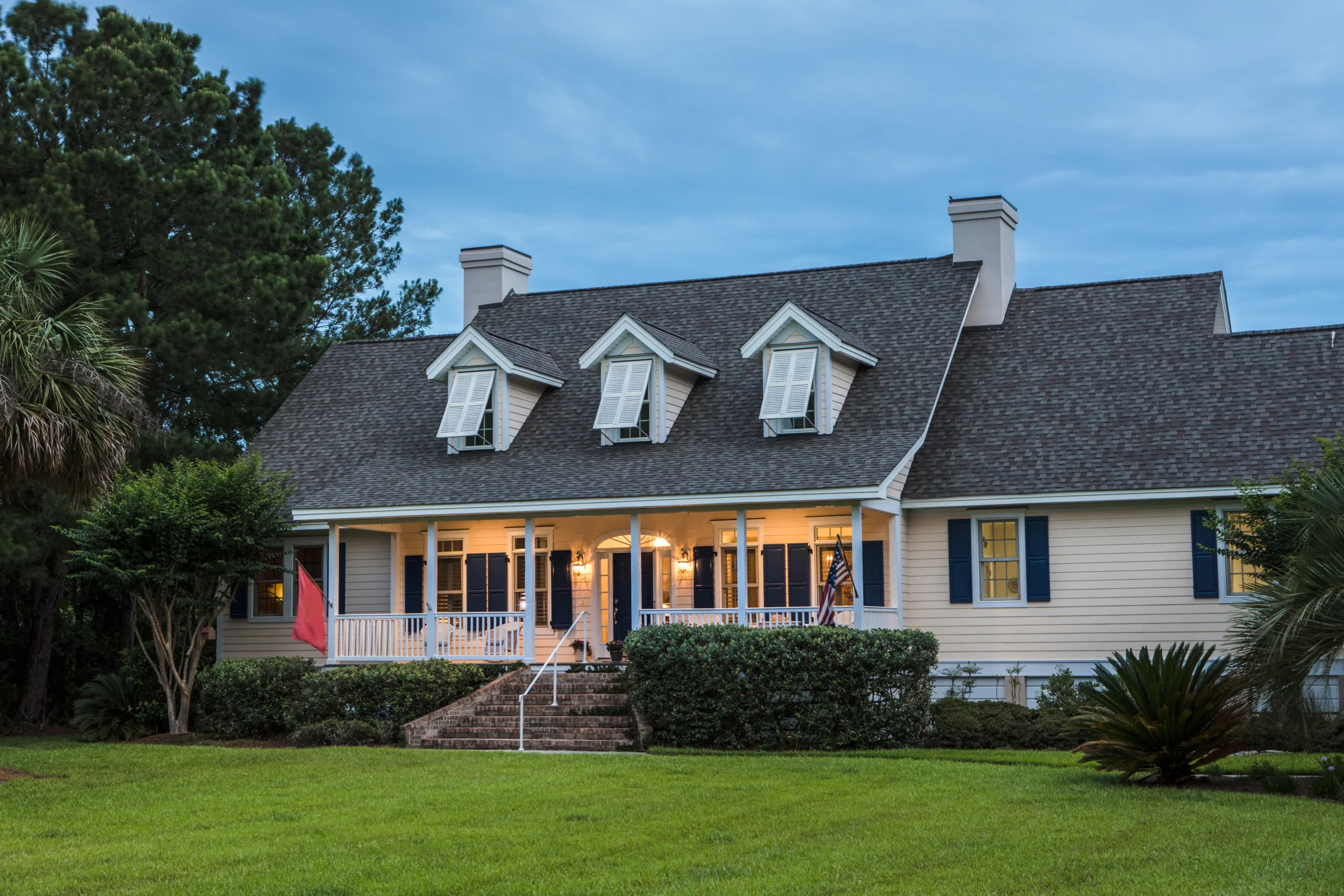 Yellow house with large shingle roof and vertical shutters on windows