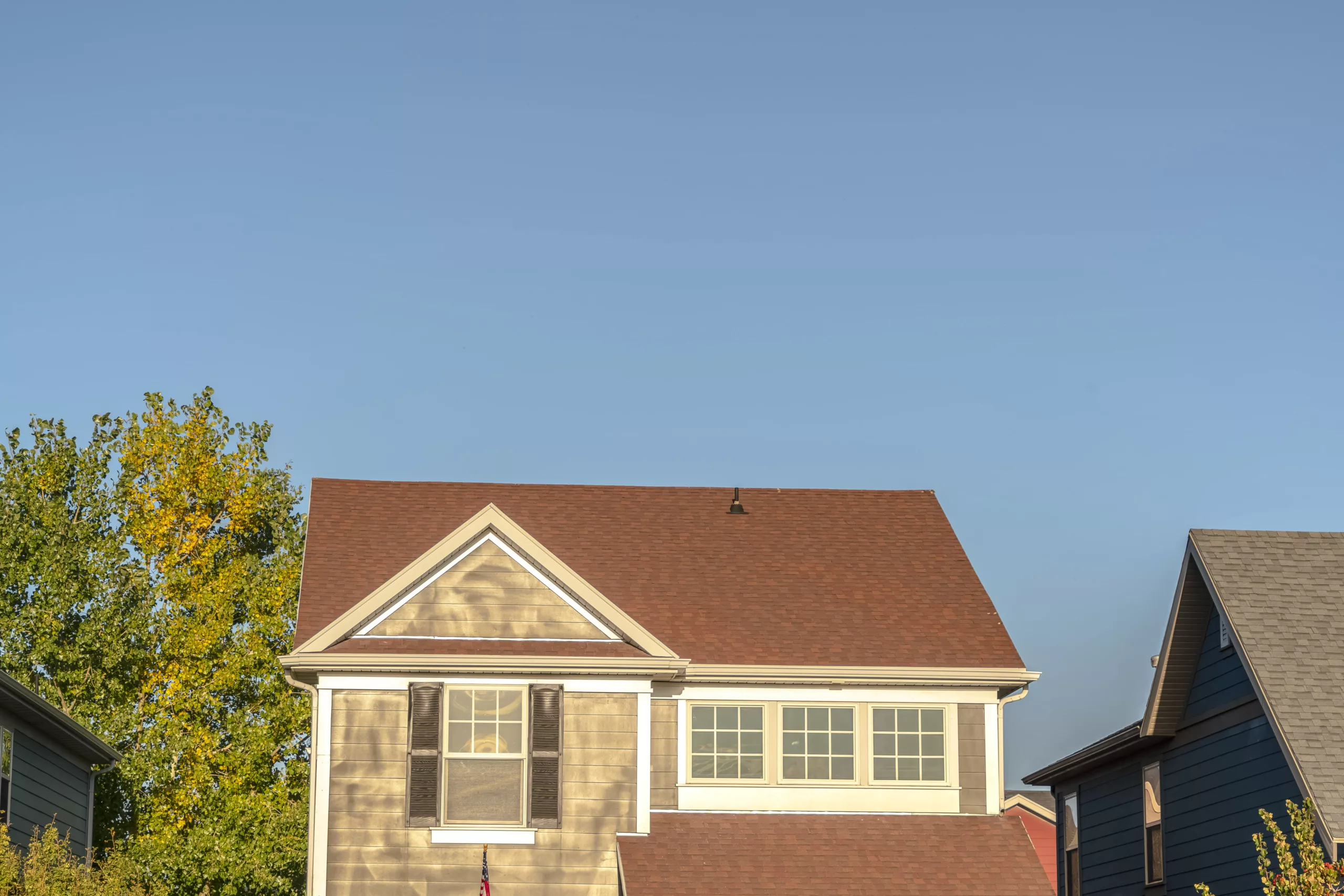 A brown-tan house features a dark red roof