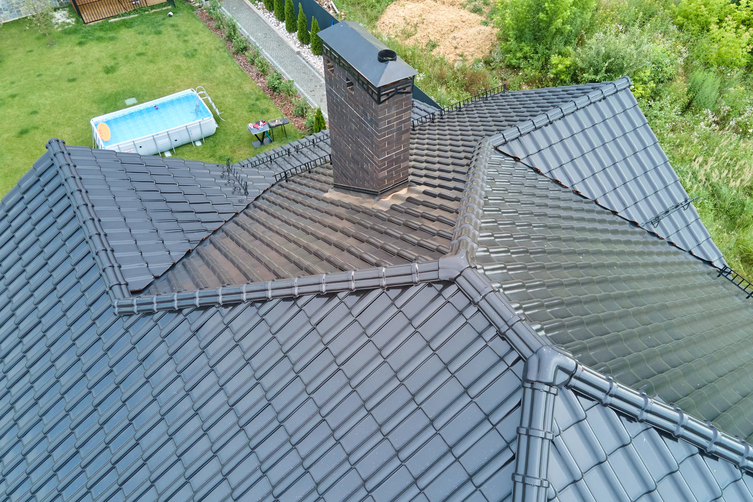 The image is from above the house showing a black metal roof with a grass backyard that has an above-ground pool.