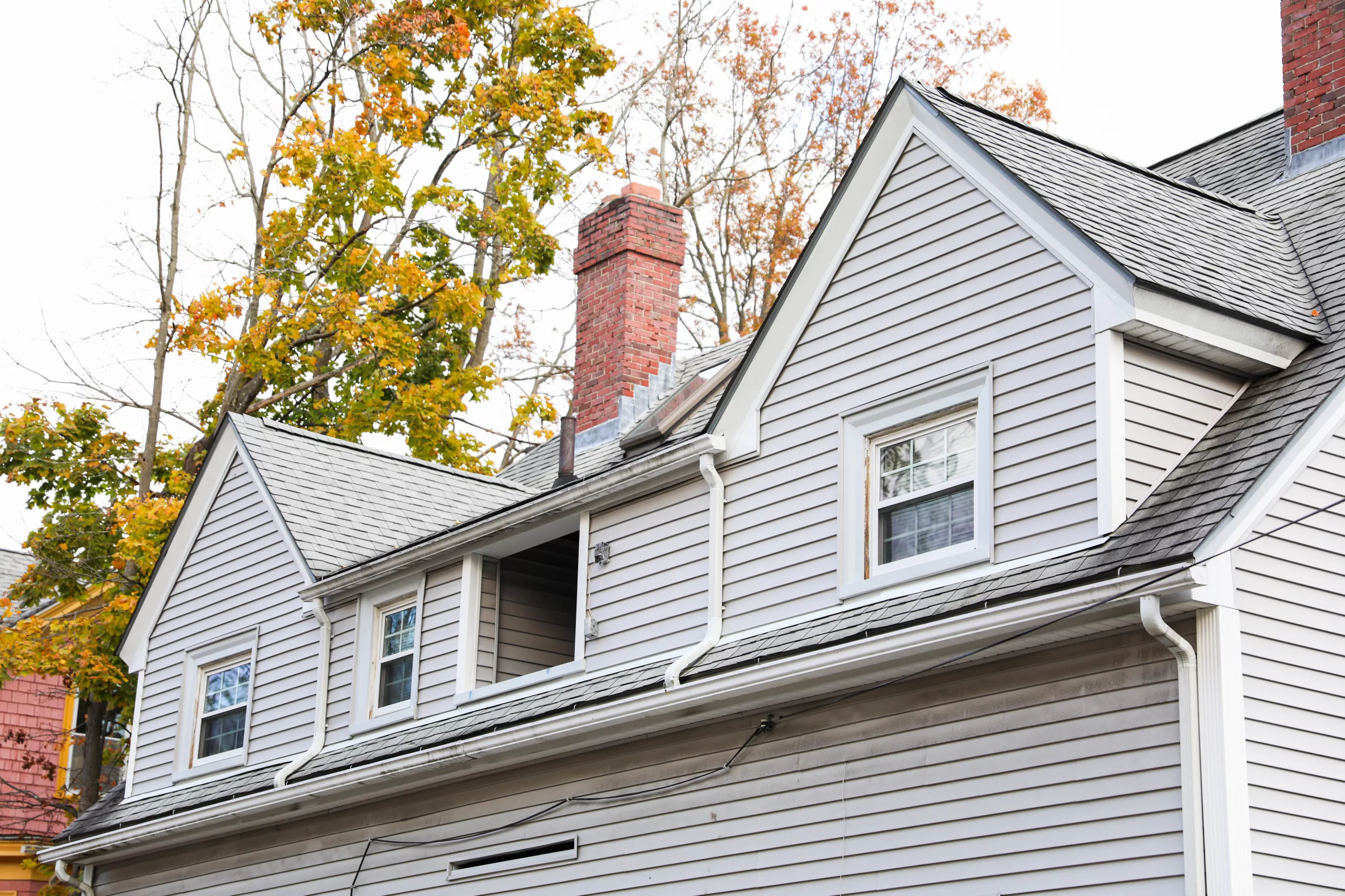 A light grey 2-story house featuring white flashing around a dark grey roof