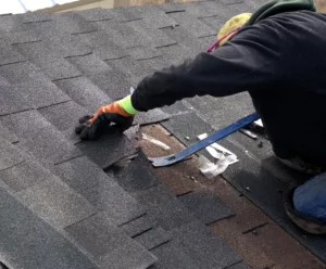 Roofer pulling up asphalt shingle during roof repair