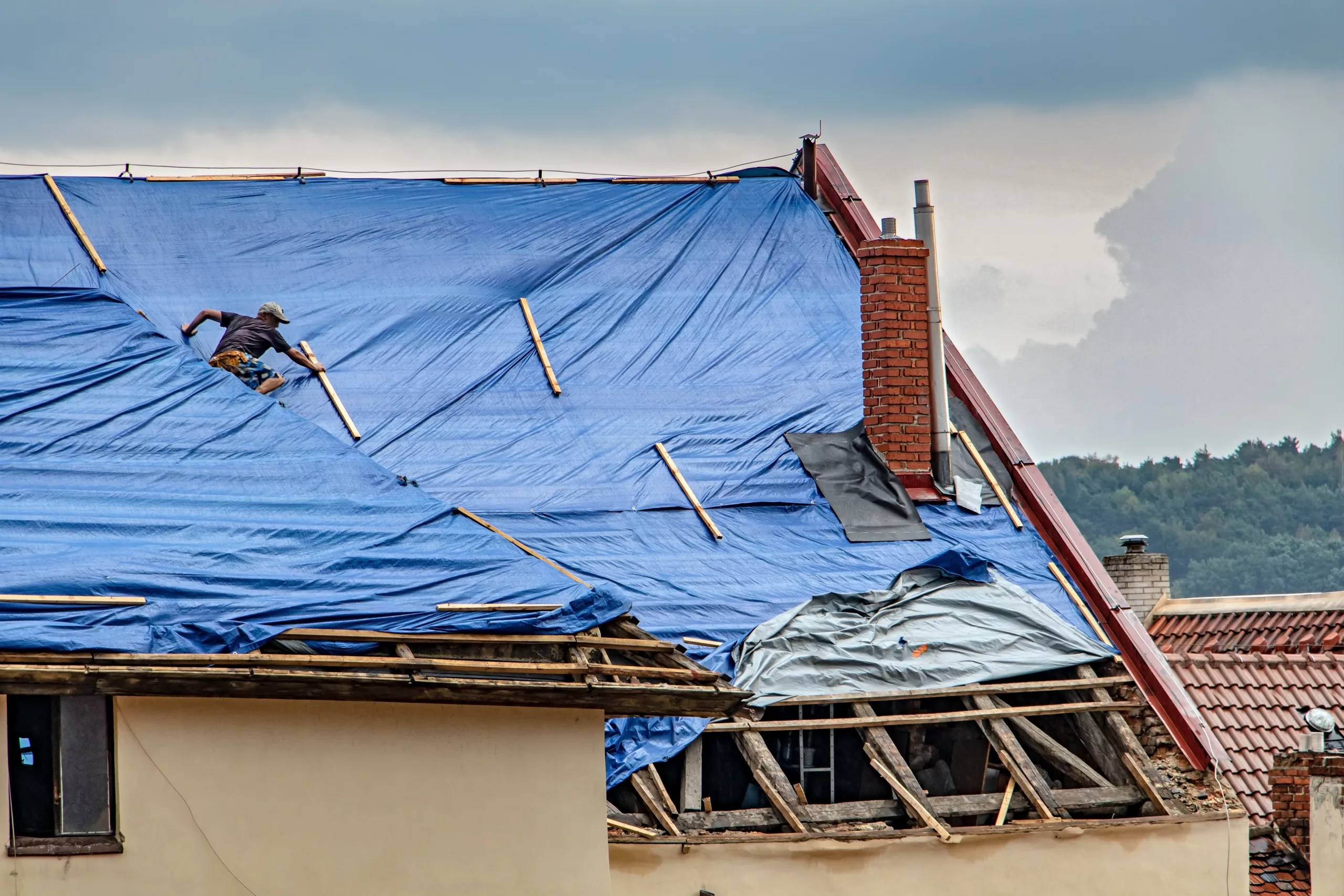 Roofer making repairs on roof with tarp on it