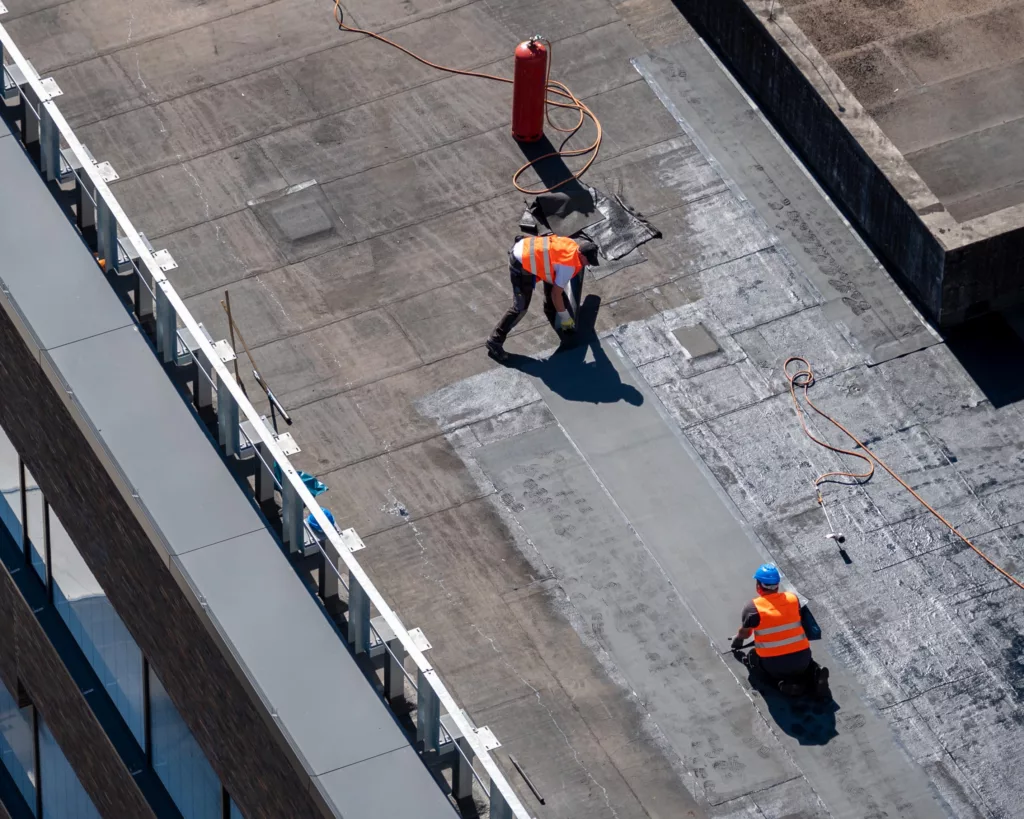 Aerial view of roofers performing flat roof repair on commercial building
